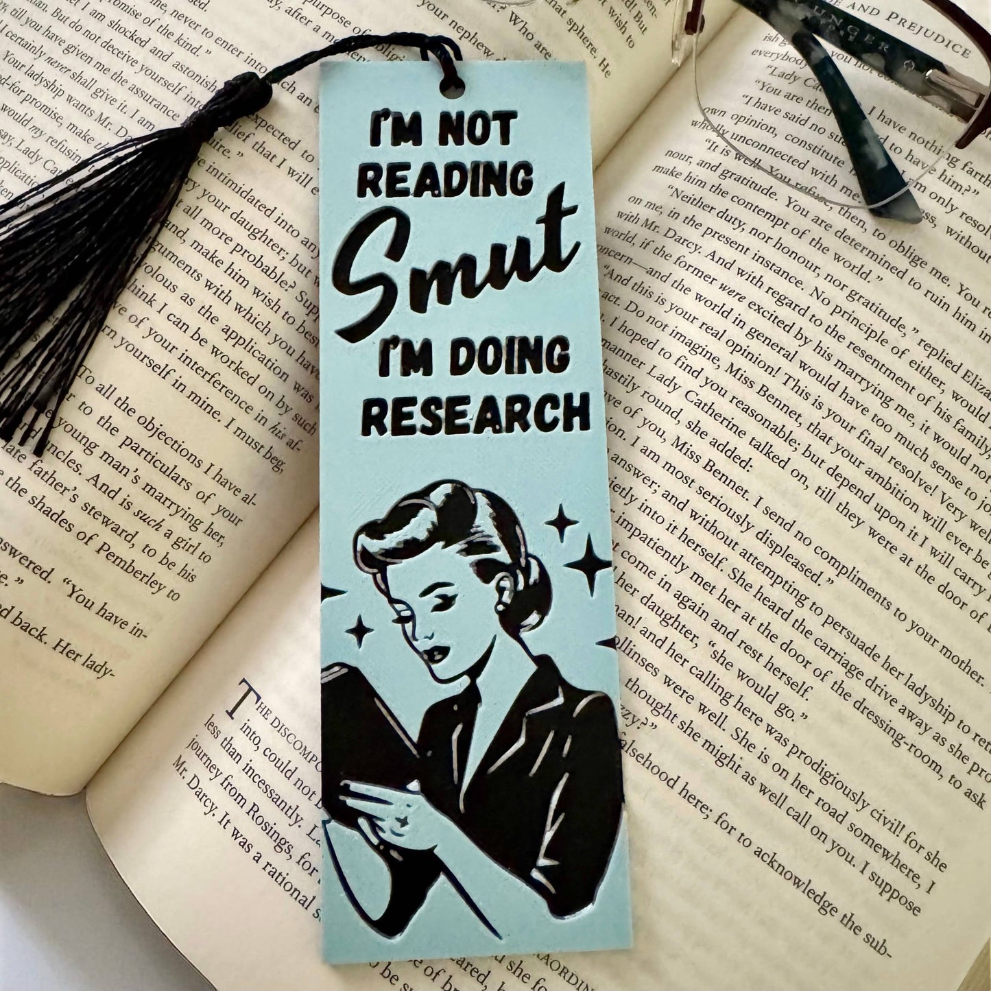 Bookmark with a vintage-style illustration of a woman and text 'I'm not reading smut, I'm doing research' on an open book.