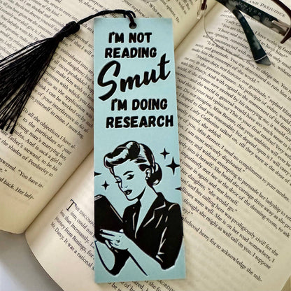 Bookmark with a vintage-style illustration of a woman and text 'I'm not reading smut, I'm doing research' on an open book.