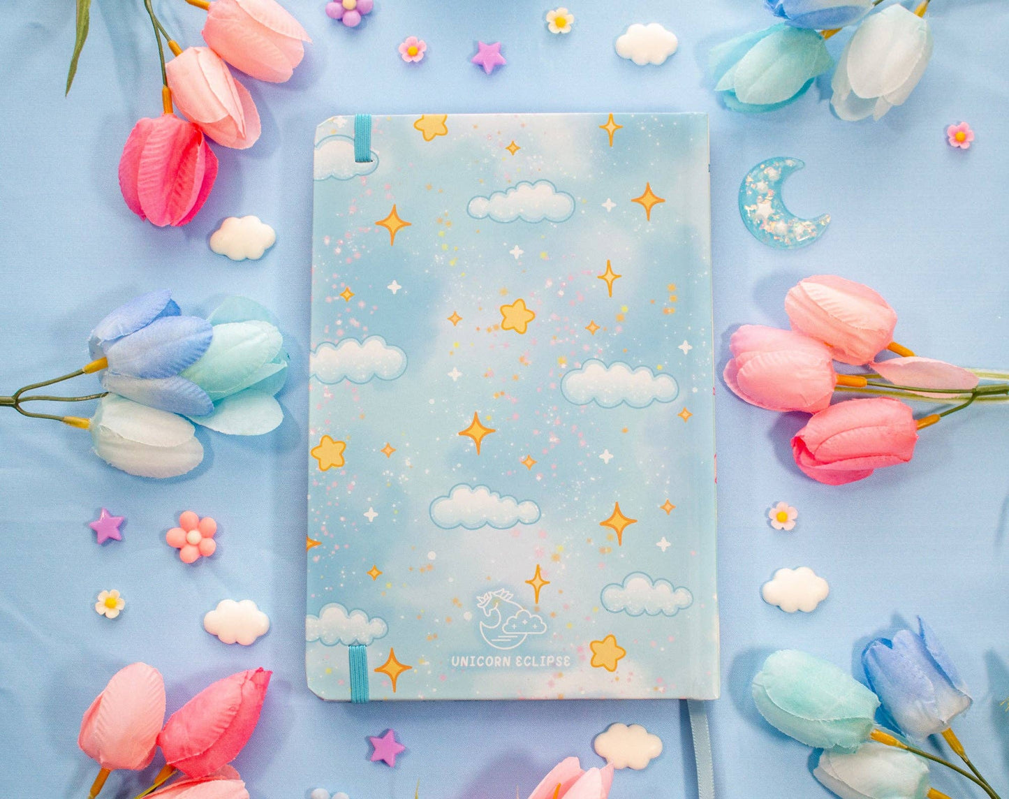 Notebook with star and cloud pattern surrounded by colorful tulips on a blue background