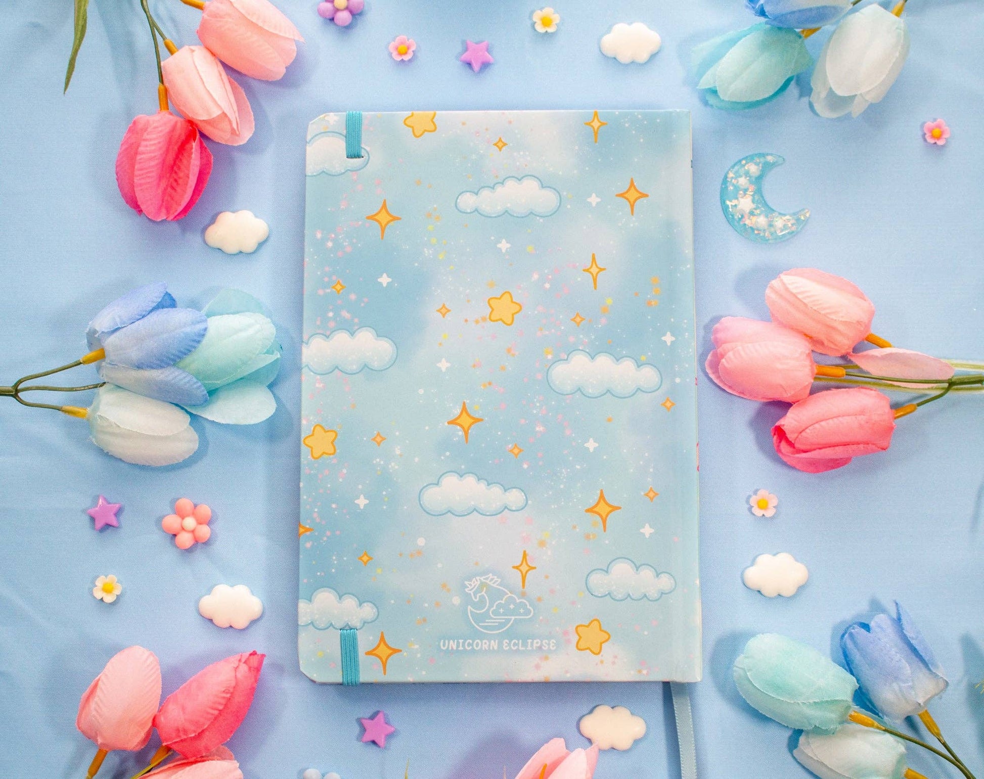 Notebook with star and cloud pattern surrounded by colorful tulips on a blue background