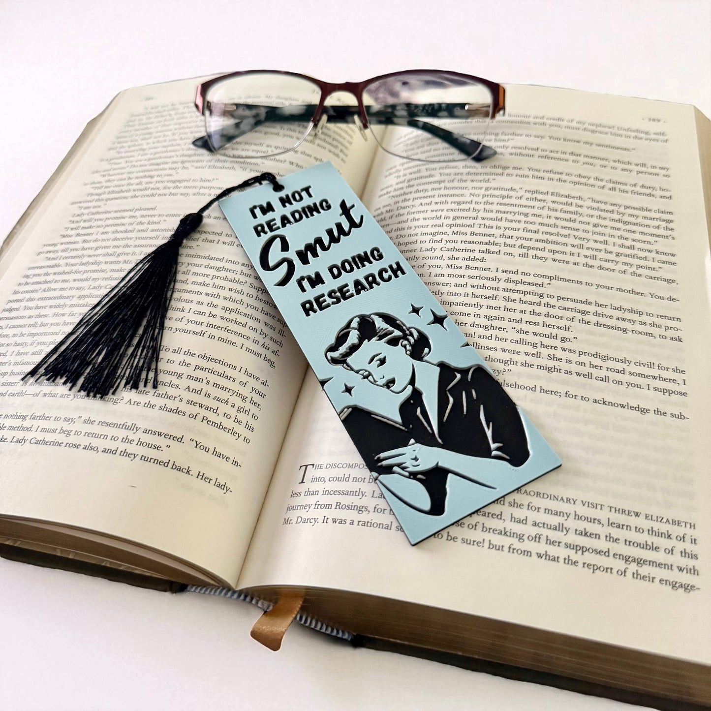 Bookmark with a tassel on an open book, featuring text and a silhouette design.