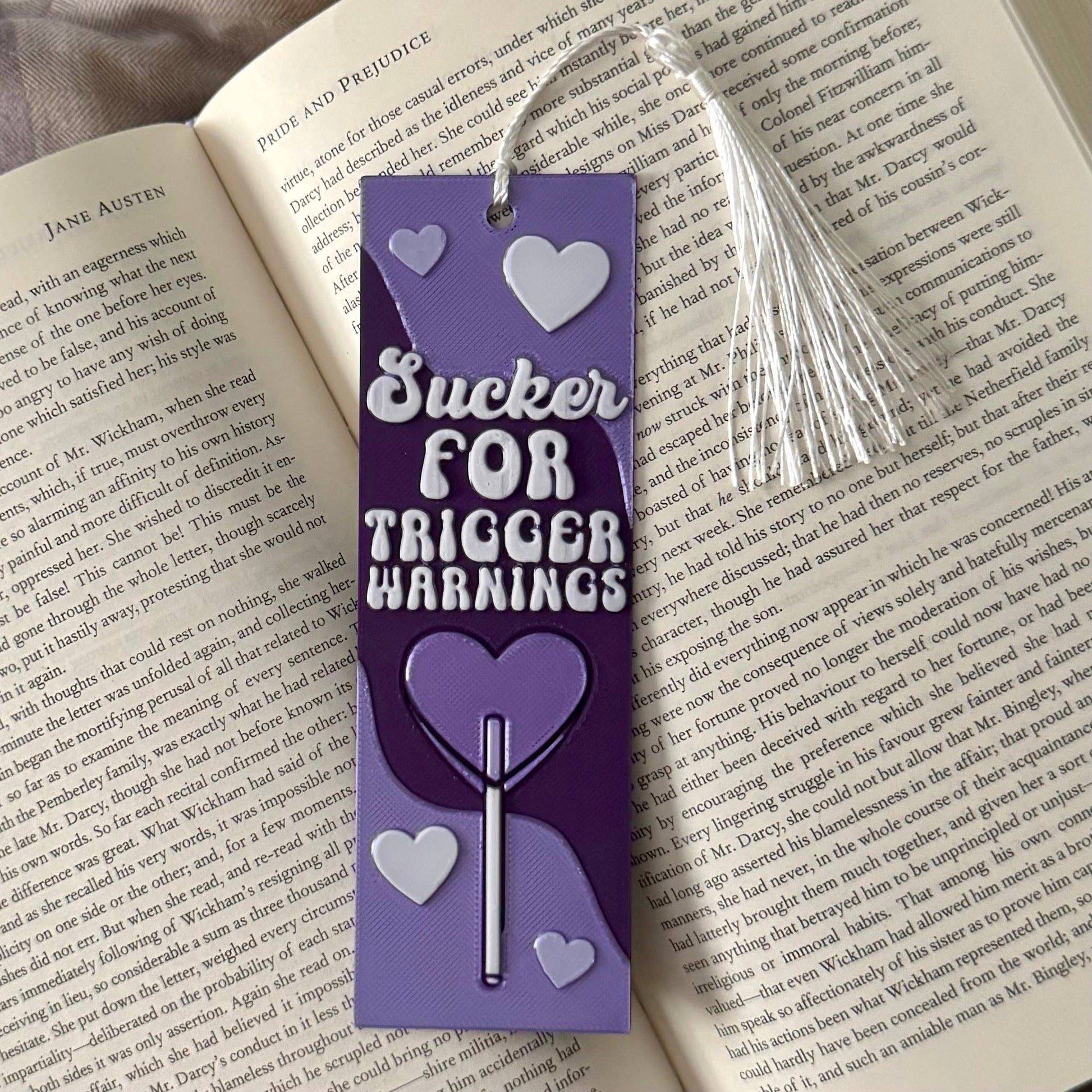 Purple bookmark with text 'Sucker for Trigger Warnings' on an open book