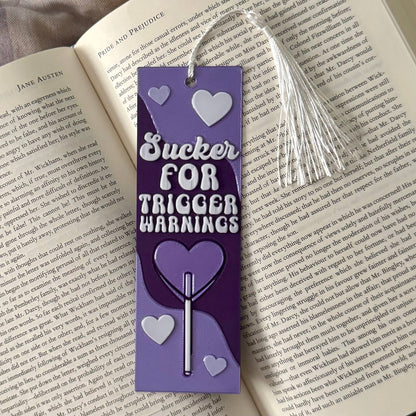 Purple bookmark with text 'Sucker for Trigger Warnings' on an open book