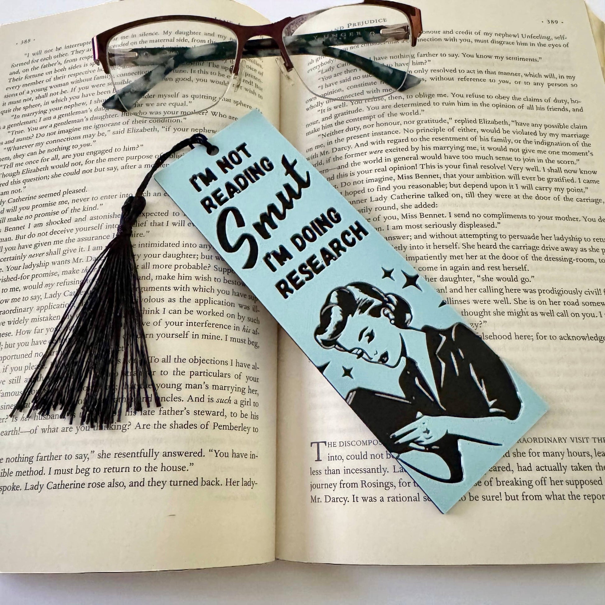 Bookmark with text 'I'm not reading smut, I'm doing research' on an open book.