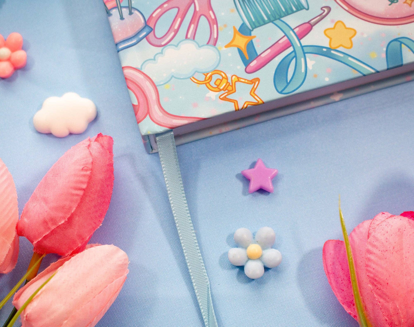 Notebook with colorful stationery design on a blue background with pink flowers and decorative items.