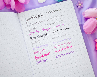 Notebook with various pen tests on a purple background with flowers